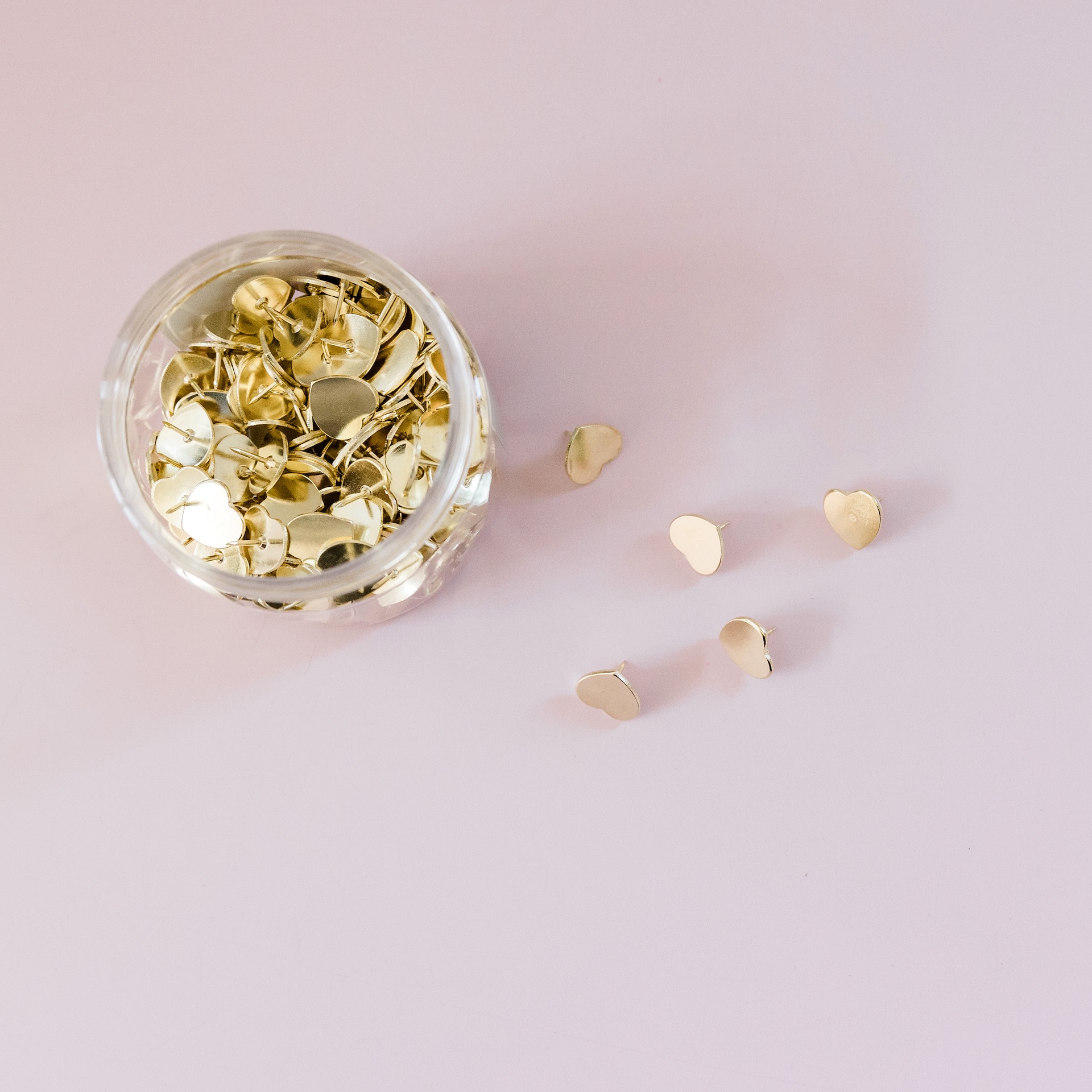 Gold pins in a glass jar on a pink background